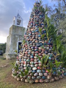 Cone shaped sculpture with painted rocks and plants growing between the rocks.